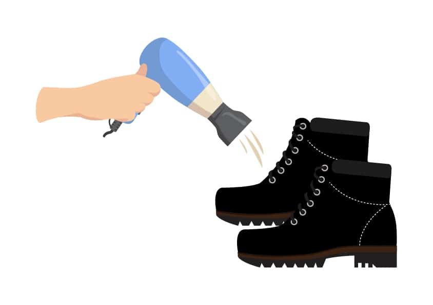 A hand holding a hairdryer warming a pair of black boots